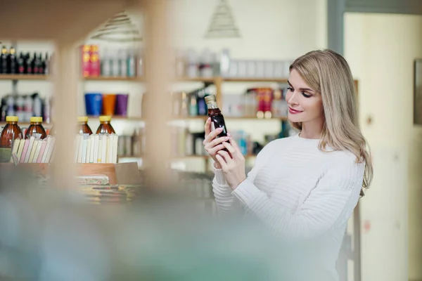 Een jonge aantrekkelijke blonde vrouw in een witte trui shopper in de winkel kiest crème. Cosmetica en schoonheidssalon. — Stockfoto
