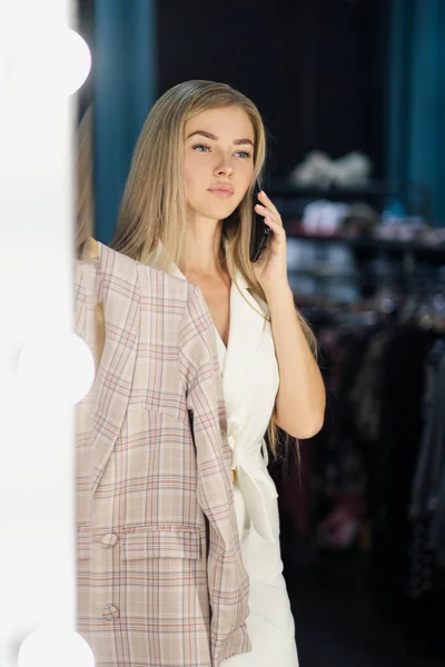 Jong mooi blond vrouw probeert en kiest een jurk in een garderobe in een winkel boetiek. — Stockfoto