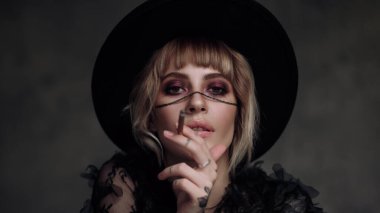 Siyah şapkalı ve elbiseli güzel sarışın kadın. Gri arkaplanda bir portre.