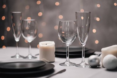 Restoranda bir masa ayarlandı. Masa servisi. Gri sanatsal arka plan. Siyah matte kaplar, cam bardaklar. Beyaz mumlar ve dekor. Arka planda şenlikli sarı ışıklar çelengi.