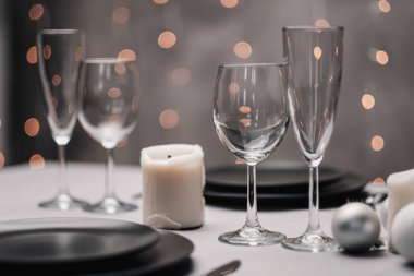 Restoranda bir masa ayarlandı. Masa servisi. Gri sanatsal arka plan. Siyah matte kaplar, cam bardaklar. Beyaz mumlar ve dekor. Arka planda şenlikli sarı ışıklar çelengi.