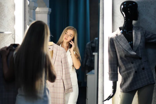 Jong mooi blond vrouw probeert en kiest een jurk in een garderobe in een winkel boetiek. — Stockfoto