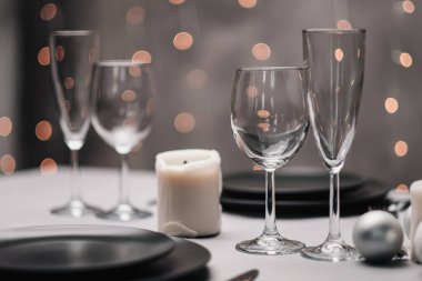 Restoranda bir masa ayarlandı. Masa servisi. Gri sanatsal arka plan. Siyah matte kaplar, cam bardaklar. Beyaz mumlar ve dekor. Arka planda şenlikli sarı ışıklar çelengi.