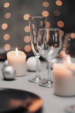 Restoranda bir masa ayarlandı. Masa servisi. Gri sanatsal arka plan. Siyah matte kaplar, cam bardaklar. Beyaz mumlar ve dekor. Arka planda şenlikli sarı ışıklar çelengi.
