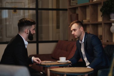 Takım elbiseli iki adam bir restoranda oturuyor. Bir iş toplantısı. Erkekler kahve içer..