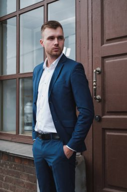 Takım elbiseli, sakallı, genç ve yakışıklı bir adam şehrin caddesinde duruyor..