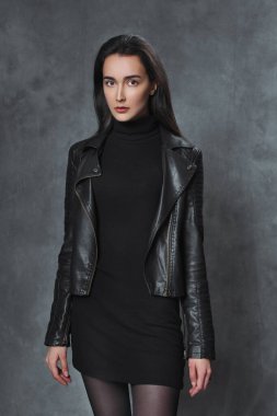 Gri arka planda siyah kazaklı ve siyah deri ceketli güzel esmer kız..