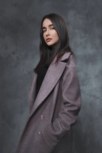Hermosa chica morena joven en un suéter negro y abrigo lila sobre un fondo gris . —  Fotos de Stock
