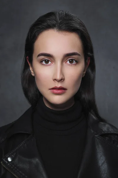 Красива молода брюнетка в чорному светрі і чорна шкіряна куртка на сірому фоні . — стокове фото