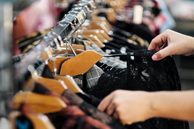 Mağazadaki askıdan elbise seçen bir kadının ellerine yakın çekim..