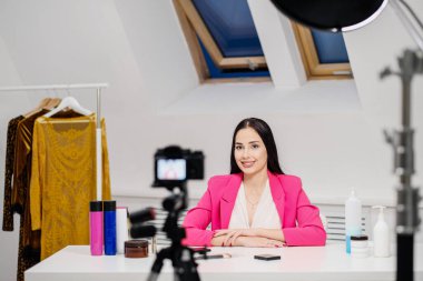 Kadın bir güzellik blogcusu beyaz bir odada video kaydediyor. Bir tripoda ışık ve kamera..