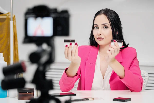 En kvinnlig skönhetsbloggare spelar in en video i ett vitt rum. Belysning och kamera på stativ. — Stockfoto