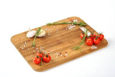 Pişmiş tütsülenmiş et beyaz bir arka planda tahta kesme tahtasının üzerinde yatar. Bitkiler ve sebzelerle süslenmiş..