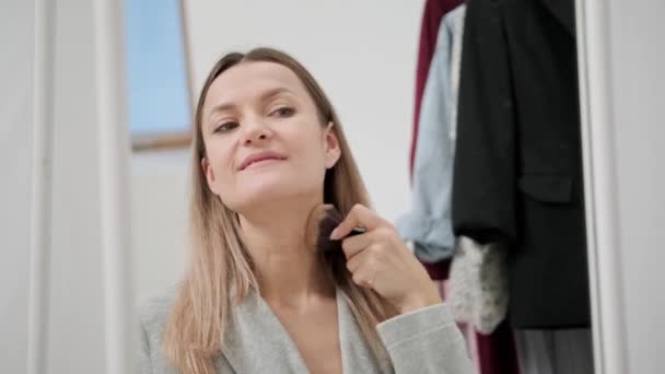 Een jonge aantrekkelijke millennial vrouw zet op make-up bij een grote spiegel thuis. — Stockvideo