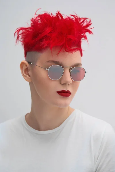 Πορτρέτο του ένα δροσερό μοντέρνο κορίτσι της μόδας. Κοντό κούρεμα με ξυρισμένο κρόταφο. Βαμμένα κόκκινα μαλλιά. Κόκκινο κραγιόν. Φωτογραφία στούντιο σε λευκό φόντο. Αναρροφητήρες και καρό παντελόνι. — Φωτογραφία Αρχείου