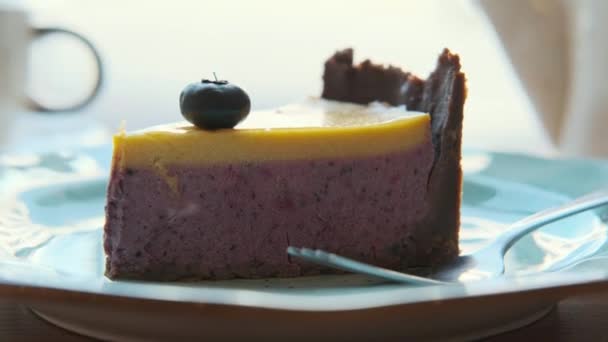 Detailní záběr šálku s čajem a zákuskem borůvkového tvarohového koláče na stole v útulné kavárně u okna. — Stock video