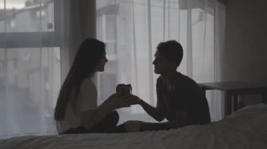 Genç bir çift, erkek ve kadın yatak odasında pencerenin yanında yerde oturuyorlar. Koca, karısına bir hediye kutusu verir. Kız sürprizin tadını çıkarıyor..