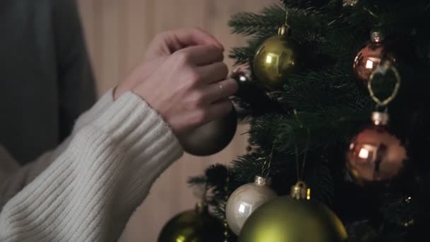 Mladý pár ve večerních hodinách zdobí vánoční stromek doma. Drž koule, obejmi se a zasměj se. Štědrý večer. — Stock video