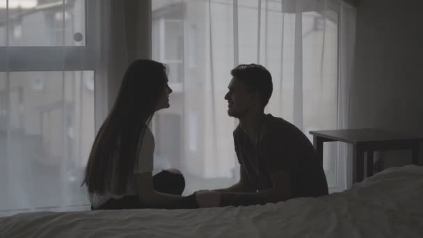 A young couple, man and woman at home in the bedroom are sitting on the floor by the window. Husband gives a gift box to his wife. The girl enjoys the surprise. — Stock Video