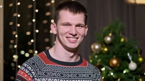 Portret van een jonge mooie man op een achtergrond van de kerstboom. — Stockvideo