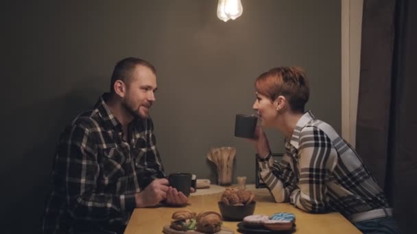 Jeune couple marié en vêtements décontractés, homme et femme, assis à la maison dans la cuisine à la table. Communication de l'âme et confort à la maison . — Video