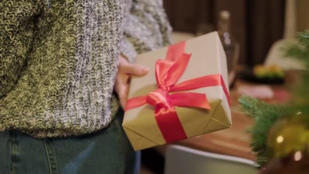Een vrouw houdt een geschenkdoos met een rood lint achter haar rug. — Stockvideo