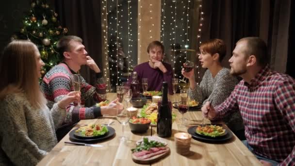 朋友们在家里围坐在桌旁享用节日宴会.庆祝圣诞节。五个人吃饭、喝香槟、说话、笑. — 图库视频影像