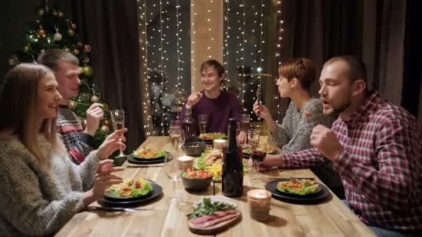 Amigos cena de fiesta en casa alrededor de la mesa. Celebra la Navidad. Cinco personas comen, beben champán, hablan y ríen . — Vídeo de stock