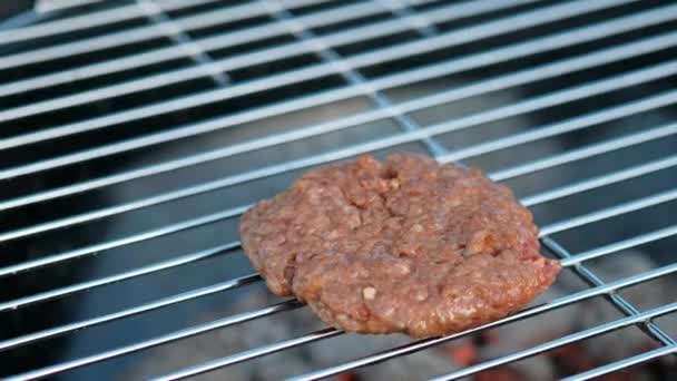 Grillsütő. Egy férfi hússzeletet és húsgombócot süt hamburgernek, megfordítja a húst fogóval.. — Stock videók