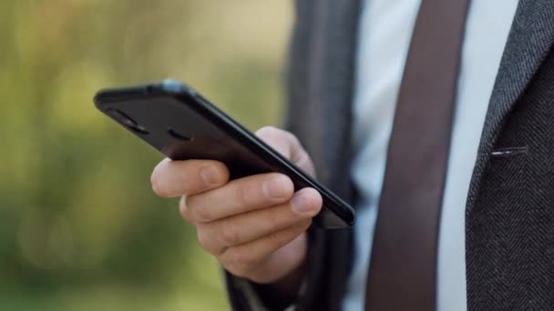 Kahverengi takım elbiseli genç çekici erkek işadamı bir cep telefonu kullanıyor. Bir mesaj yazmak ve akıllı telefondan sohbet etmek.. — Stok video