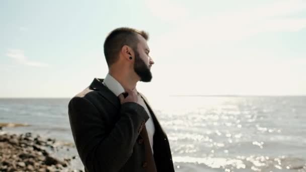Молодий привабливий чоловічий бізнесмен в коричневому костюмі з портфелем стоїть на березі моря . — стокове відео