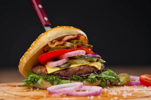 Delicioso hambúrguer suculento com carne bovina, pão e legumes em uma tábua de madeira com uma faca presa. Entrega de comida. Restaurante fast food . — Fotografia de Stock