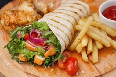 İnce hamurlu tortilla ve sebze ve salatayla pişirilmiş tavuk dürümü. Tahta kesme tahtasında patates kızartması ve sos ile servis edilir..