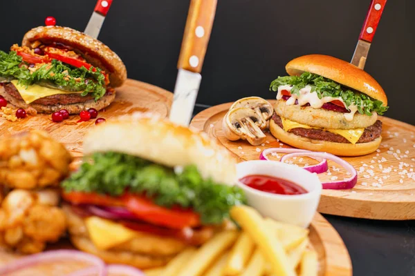 Combo set of fast food. Juicy hamburger, French fries, chicken legs and sauce. Served wooden board and cutlery on a black background. Fast food restaurant. Food delivery. — Stock Photo, Image