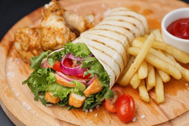 İnce hamurlu tortilla ve sebze ve salatayla pişirilmiş tavuk dürümü. Tahta kesme tahtasında patates kızartması ve sos ile servis edilir..