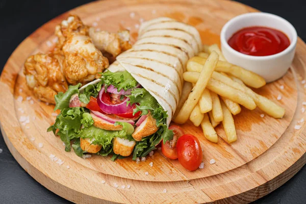 Chicken roll, cooked on fire in a thin dough tortilla with vegetables and salad. Served serve with cutlery on a wooden cutting board with French fries and sauce.