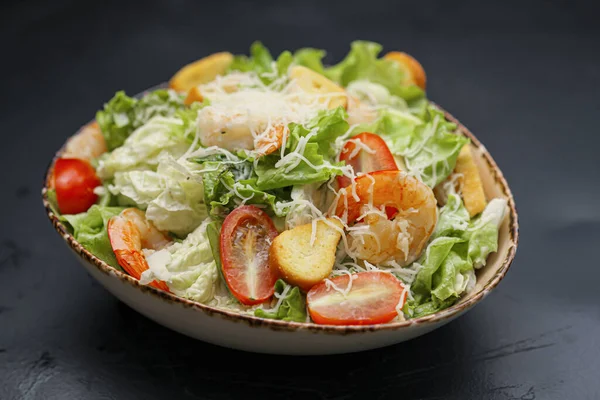 Caesar salat med rejer i en skål på en sort baggrund. - Stock-foto