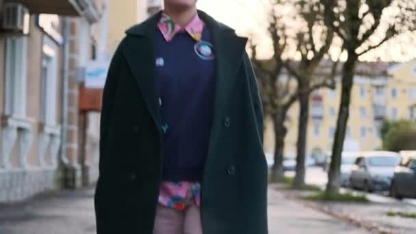 Una joven mujer inteligente con un corte de pelo corto y teñido de pelo, con un abrigo verde y un suéter con estampados en la calle de la ciudad . — Vídeo de stock