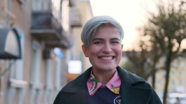 一个年轻聪明的女人，剪短头发，染成彩色头发，穿着绿色外套，穿着印有城市街道上指纹的毛衣. — 图库视频影像