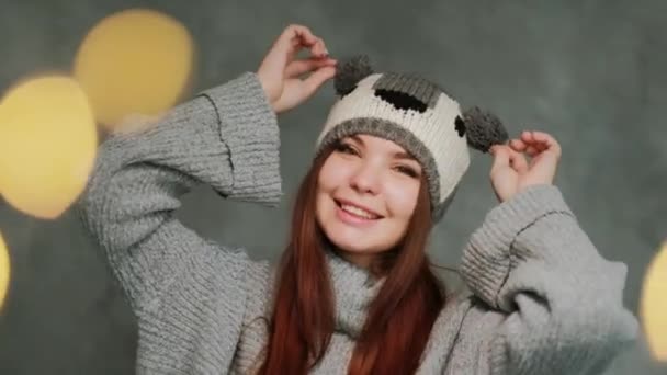 Atrakcyjna dziewczyna w dzianinie zimowy sweter i kapelusz z koalą bawi się i pozuje na szarym tle. — Wideo stockowe
