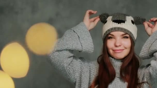 Chica atractiva en un suéter de punto de invierno y un sombrero con un koala se divierte y posa sobre un fondo gris . — Vídeo de stock