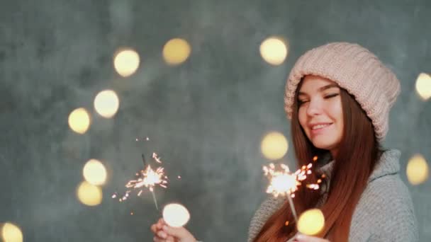 Roztomilá dívka v teplém svetru a pleteném klobouku zapálí jiskry a raduje se. Rozmazaná světla. — Stock video