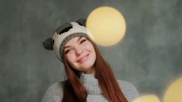 Chica atractiva en un suéter de punto de invierno y un sombrero con un koala se divierte y posa sobre un fondo gris . — Vídeos de Stock