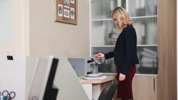 A young woman in a jacket, an office worker prints documents on a copy machine. — Stock Video