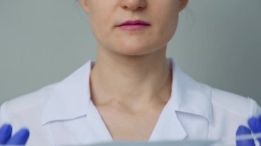 Beyaz cüppeli ve eldivenli genç bir kadın doktor yüzüne koruyucu bir maske takıyor..