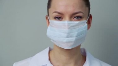 Beyaz cüppeli ve eldivenli genç bir kadın doktor yüzüne koruyucu bir maske takıyor..