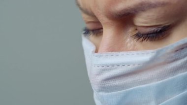 Beyaz cüppeli, maskeli ve eldivenli bir kadın doktor. Yüzü yakın plan. Doktor ağlar ve dua eder. Gözyaşları. Salgın ve virüs salgını. Coronavirus covid-19.