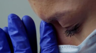 Beyaz cüppeli, maskeli ve eldivenli bir kadın doktor. Yüzü yakın plan. Doktor ağlar ve dua eder. Gözyaşları. Salgın ve virüs salgını. Coronavirus covid-19.