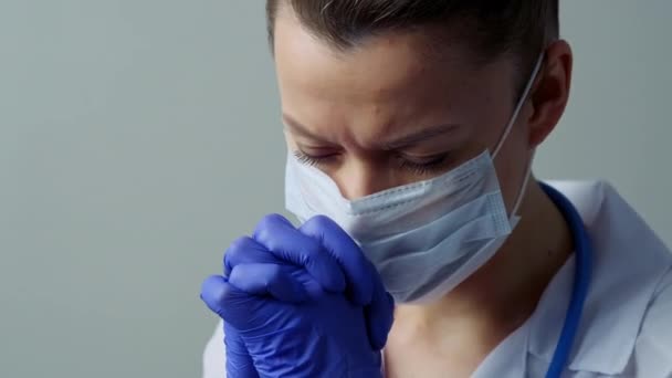 Жіночий лікар-терапевт у білому халаті, масці та рукавичках. Обличчя крупним планом. Лікар плаче і молиться. Сльози в очах. Пандемія та епідемія вірусів. Коронавірус коїд-19 . — стокове відео