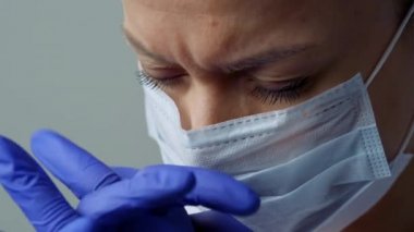 Beyaz cüppeli, maskeli ve eldivenli bir kadın doktor. Yüzü yakın plan. Doktor ağlar ve dua eder. Gözyaşları. Salgın ve virüs salgını. Coronavirus covid-19.
